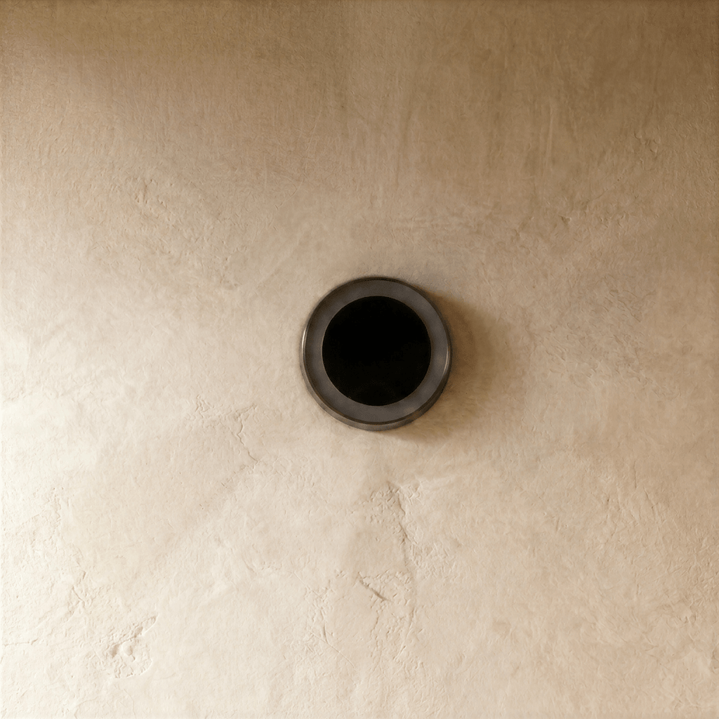 Clérachic small round solar light switched off on plaster, showing its dark solar panel in a slim steel ring.