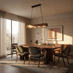 Clérachic timber bar pendant with black iron straps lit over a long walnut dining table in a sunlit room with sheer curtains.