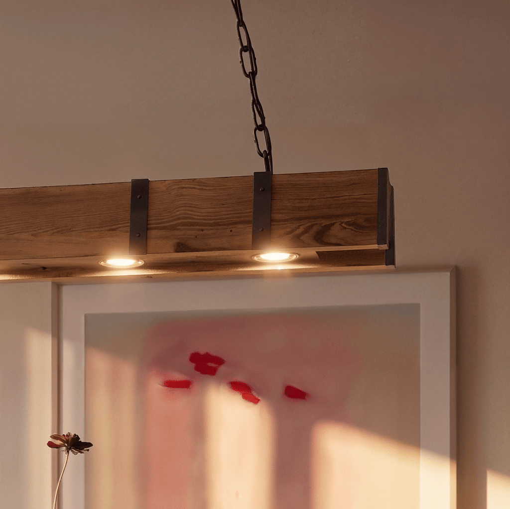 Clérachic close-up of the weathered timber beam with black iron straps and two warm bulbs set into its underside.