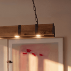 Clérachic close-up of the weathered timber beam with black iron straps and two warm bulbs set into its underside.