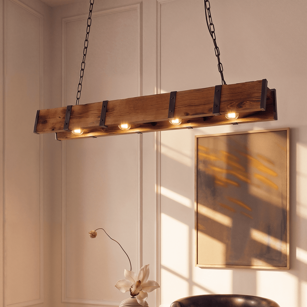 Clérachic timber beam pendant with riveted black iron straps and four lit bulbs, hung on chains beside a framed abstract print.