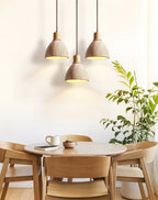 A trio of Clérachic travertine pendants at different heights above a round wooden table, with a leafy green plant beside the window.