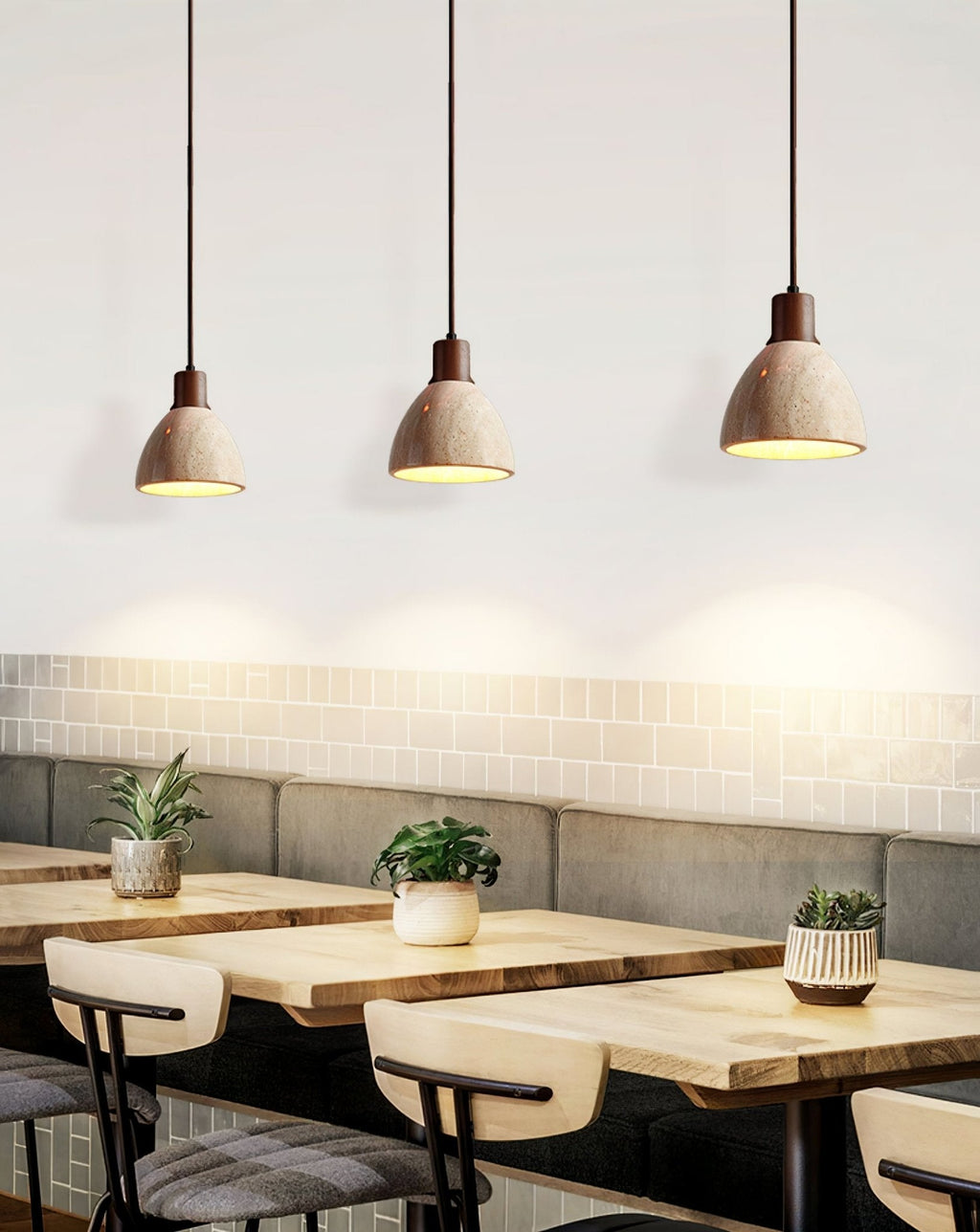 Three Clérachic pendants with dark collars in a row above a café banquette, their travertine domes casting pools of light on the wall.