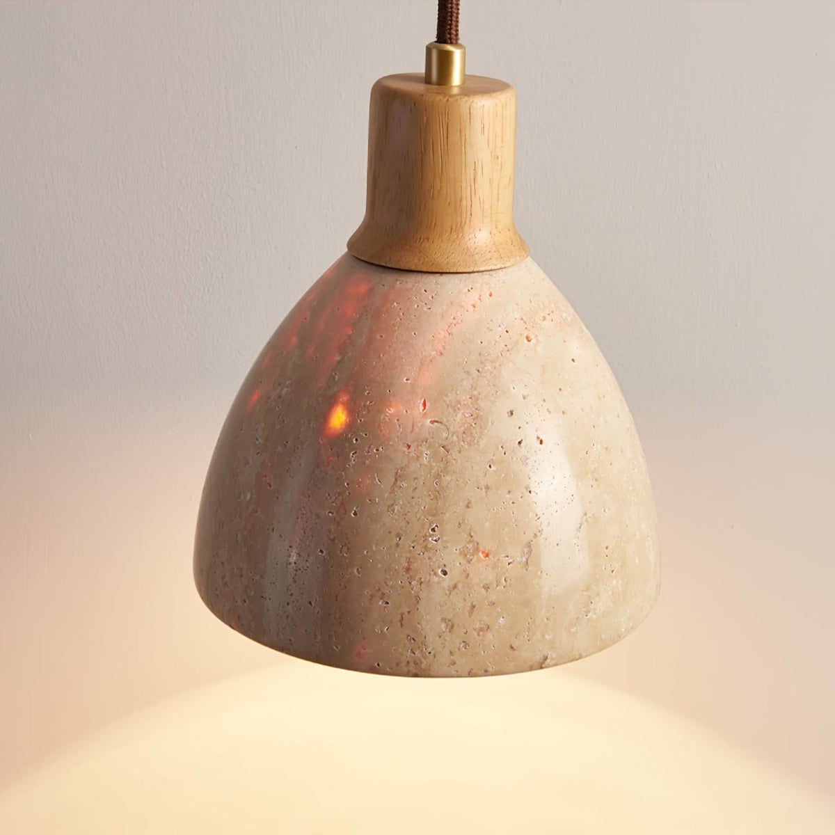 Close view of a pale wood collar and the pitted travertine dome of this Clérachic pendant, glowing warm against a soft wall.