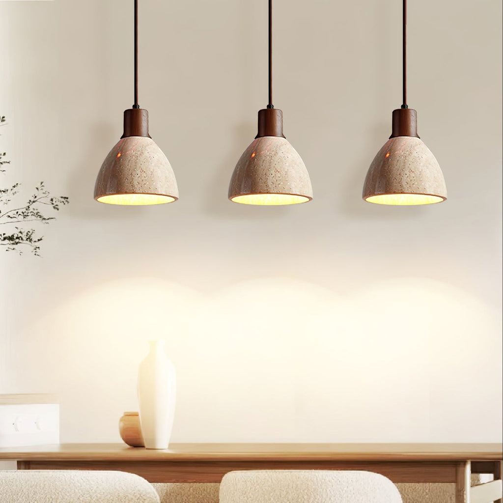 Three Clérachic pendants with dark walnut collars above a dining table, their travertine domes lit and glowing against a cream wall.