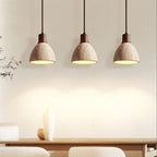 Three Clérachic pendants with dark walnut collars above a dining table, their travertine domes lit and glowing against a cream wall.