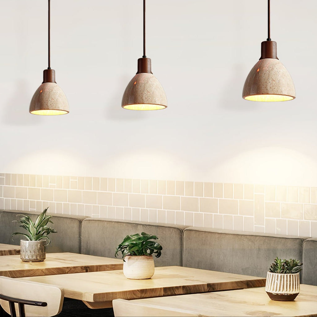 A row of three Clérachic pendants with dark collars above a café table with small potted plants and a grey banquette behind.