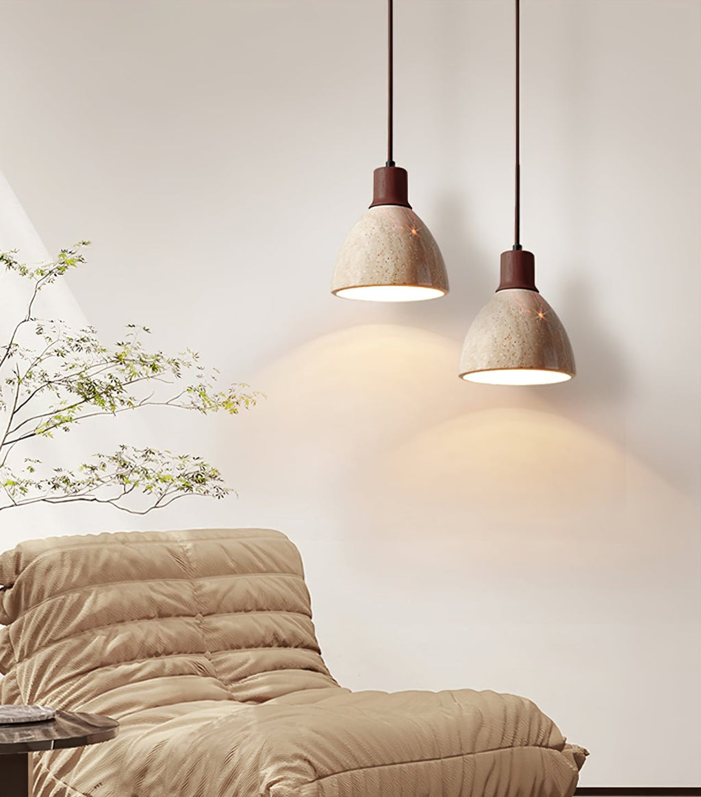 Two Clérachic pendants, one with a pale collar and one with a dark walnut collar, hung at different heights over a tan quilted sofa.