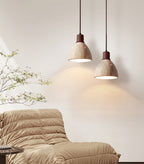 Two Clérachic pendants, one with a pale collar and one with a dark walnut collar, hung at different heights over a tan quilted sofa.
