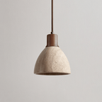 This Clérachic pendant with a dark walnut collar unlit on a plain greige backdrop, the pitted travertine dome seen from the side.