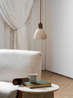 This Clérachic pendant beside a lace curtain, above a cream armchair, with a cup and a book on a round side table below.
