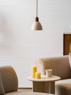 A Clérachic pendant with a dark collar in a room with beige armchairs, a round side table and two yellow pillar candles.