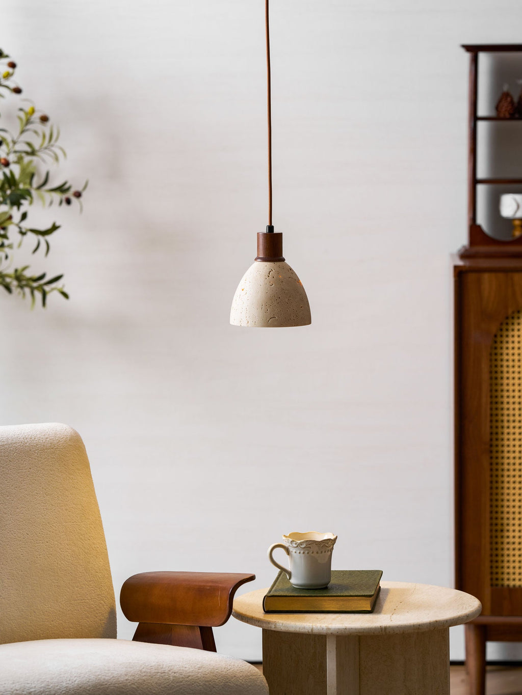 This Clérachic pendant in front of a cane-fronted wooden cabinet, above an armchair and a side table with a cup and a book.