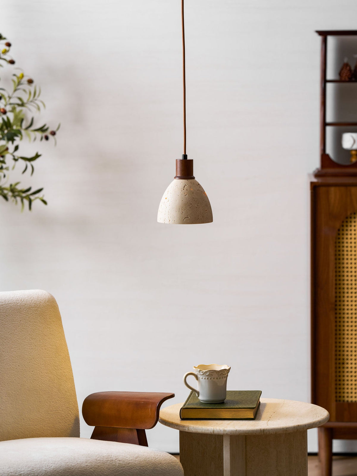 This Clérachic pendant in front of a cane-fronted wooden cabinet, above an armchair and a side table with a cup and a book.