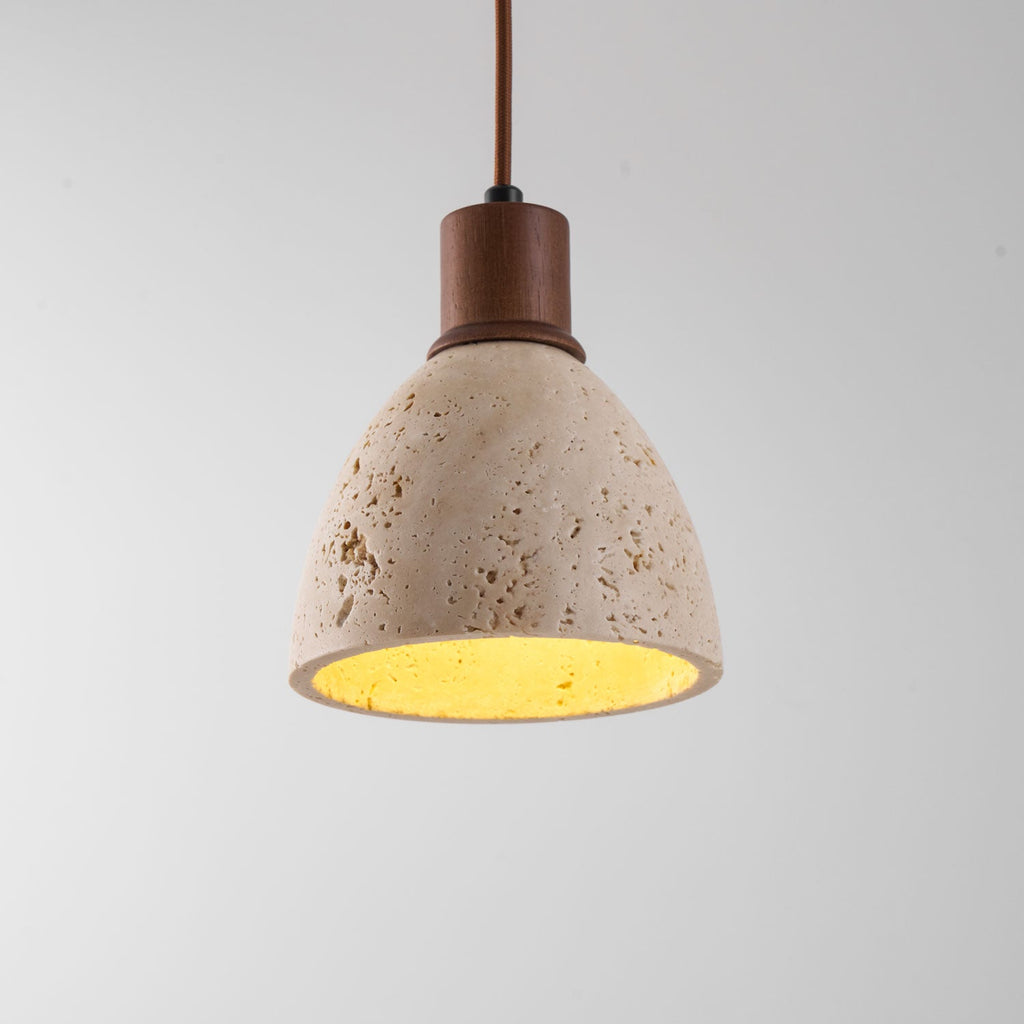 Close view of the pitted travertine dome and dark walnut collar of this Clérachic pendant, the inner surface glowing yellow.