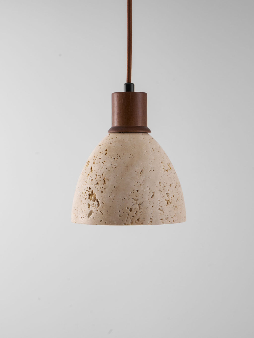 This Clérachic pendant unlit against a grey backdrop, showing the natural pores and veining of the travertine dome and the walnut collar.