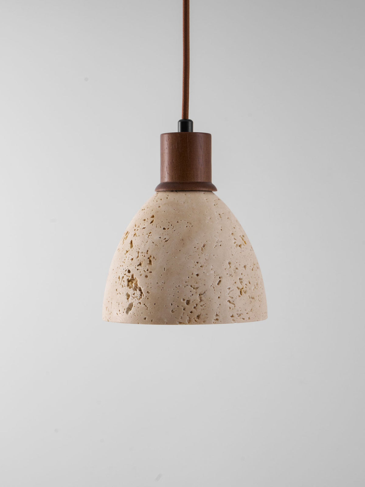 This Clérachic pendant unlit against a grey backdrop, showing the natural pores and veining of the travertine dome and the walnut collar.