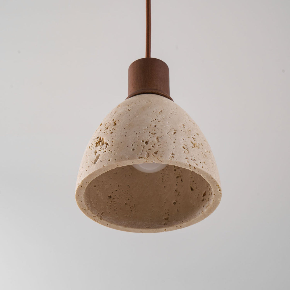 Looking up into the travertine dome of this Clérachic pendant, with the bare bulb visible and a dark walnut collar above.