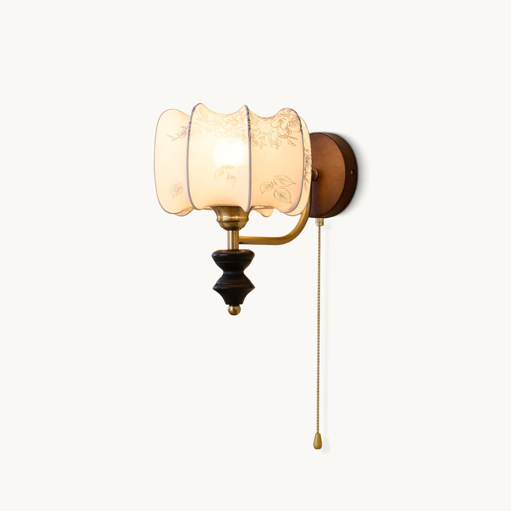 This Clérachic wall light on a plain backdrop, with a printed fabric drum shade, a brass arm, a dark turned wood pendant and a pull chain.
