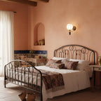 A Clérachic globe wall light above a wrought-iron bed in a peach-washed bedroom with a patterned throw.