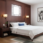 Pair of Clérachic drum-shade wall lights flanking a dark wood bedhead, with white bedding and a lattice window behind.