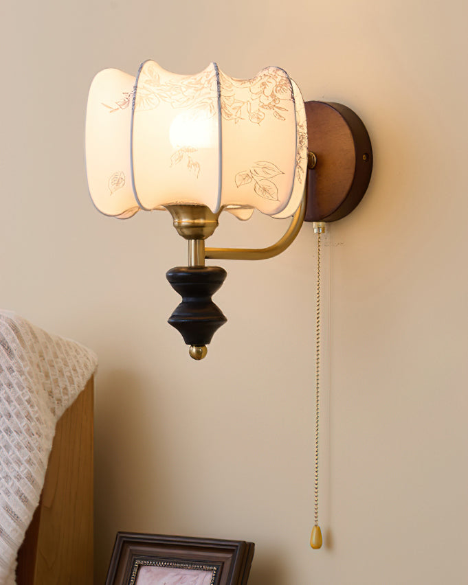Close view of the printed drum shade on this Clérachic wall light, with its scalloped edge, brass arm and wood backplate.