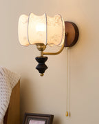 Close view of the printed drum shade on this Clérachic wall light, with its scalloped edge, brass arm and wood backplate.
