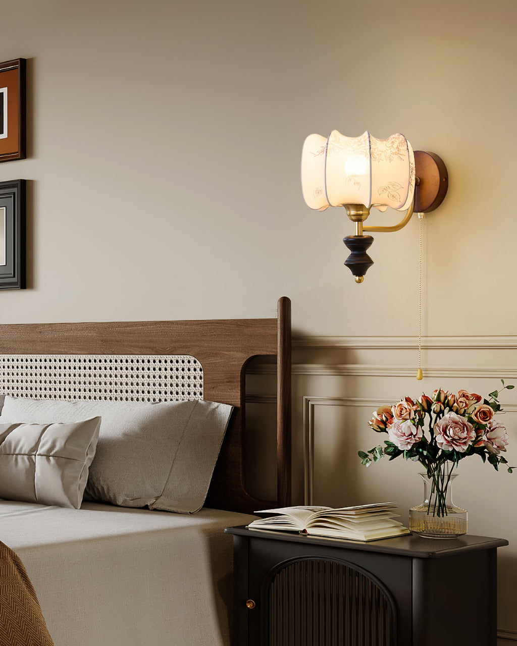 Clérachic wall light with a drum shade lit beside a bed and a rattan headboard, with pink roses and a book on the nightstand.
