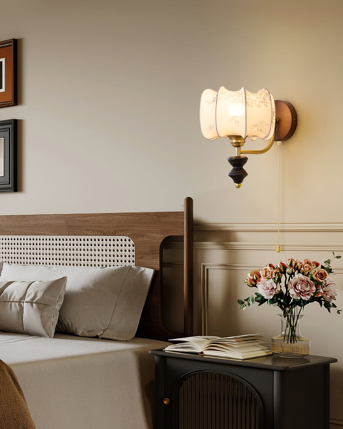 Clérachic wall light with a drum shade lit beside a bed and a rattan headboard, with pink roses and a book on the nightstand.