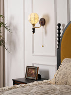 Clérachic globe wall light on a white panelled wall above a black nightstand, with a framed picture and a floral duvet below.
