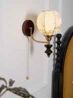 Side view of a Clérachic globe wall light, with a dark wood backplate, a brass arm and a pull chain hanging down.