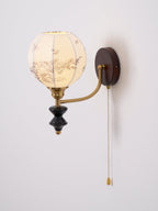 Clérachic globe wall light with a floral-printed fabric shade, brass arm and black wood pendant on a pale wall.