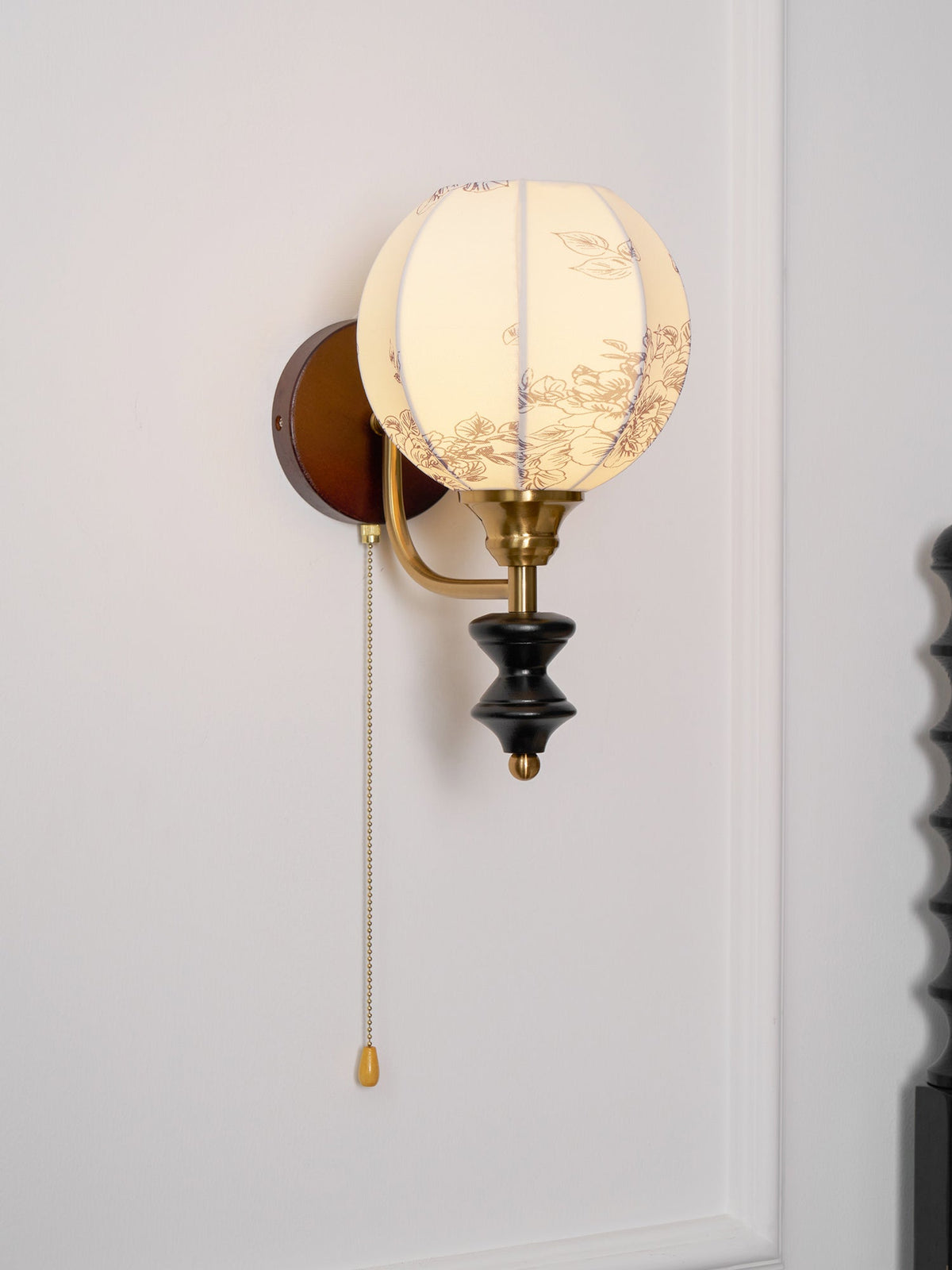 Clérachic globe wall light with a floral-printed shade, seen from a slight angle against a white panelled wall.