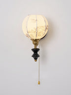Lit Clérachic globe wall light with a pull chain and a floral-printed shade against a pale wall.