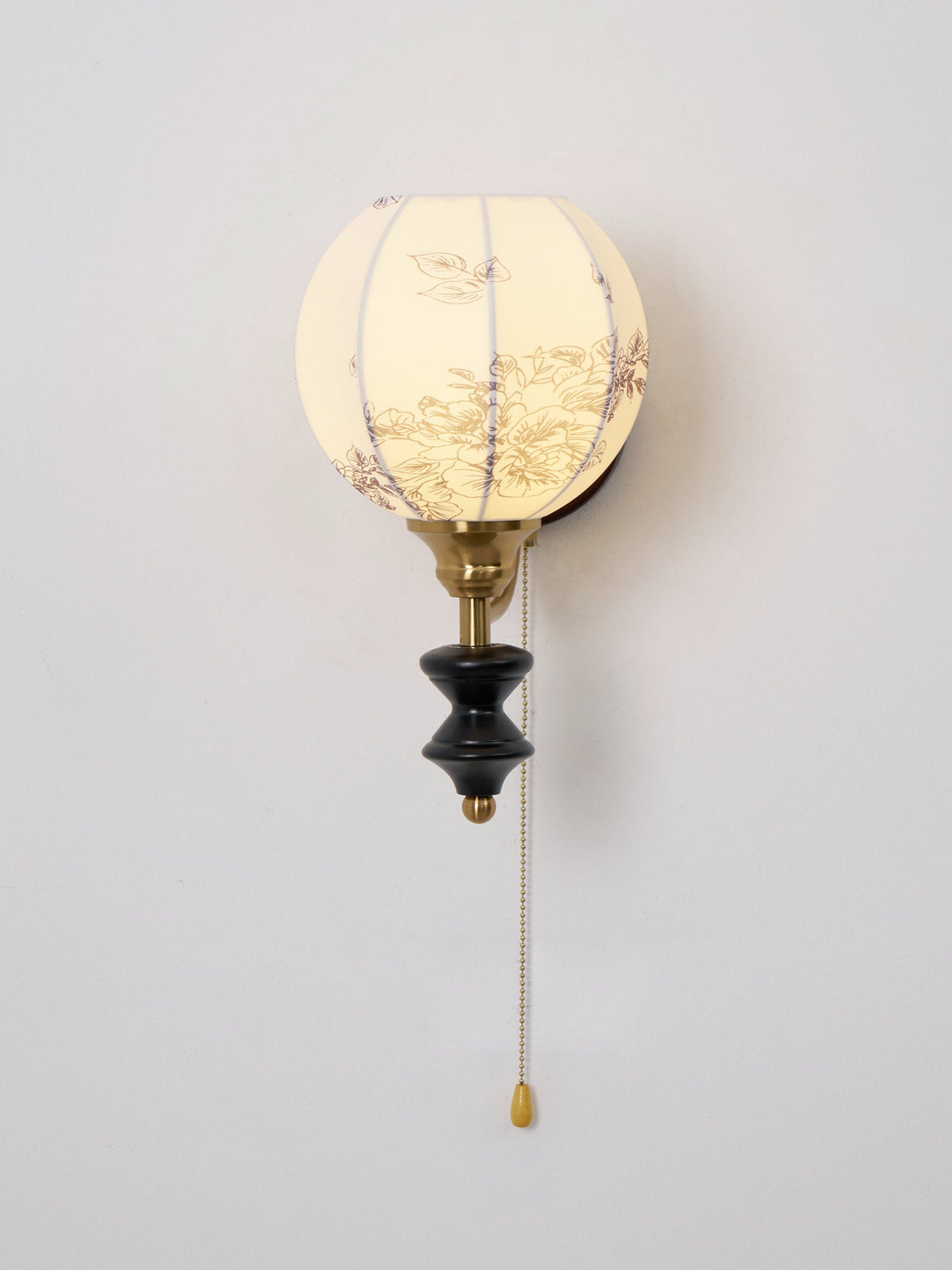 Lit Clérachic globe wall light with a pull chain and a floral-printed shade against a pale wall.