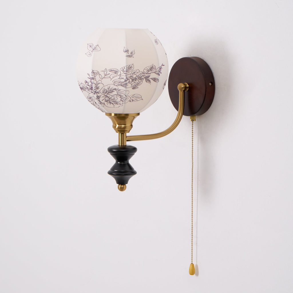 Unlit Clérachic globe wall light with a floral-printed white shade, a brass arm and a dark wood backplate.