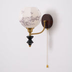 Unlit Clérachic globe wall light with a floral-printed white shade, a brass arm and a dark wood backplate.