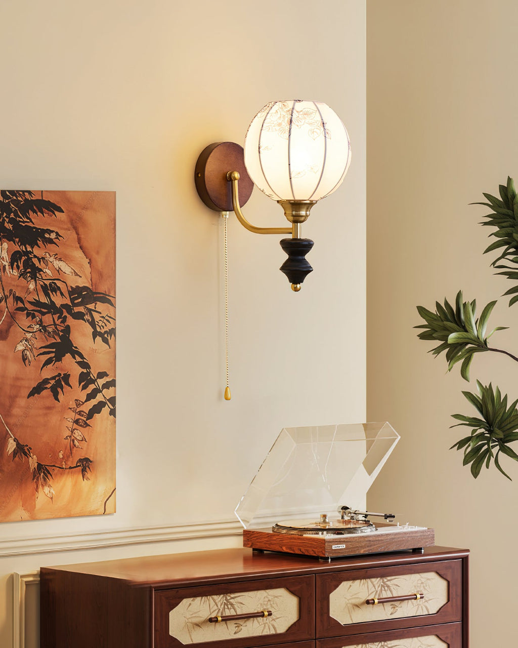 Clérachic globe wall light lit beside a leafy painting, with a record player on a wooden cabinet below.