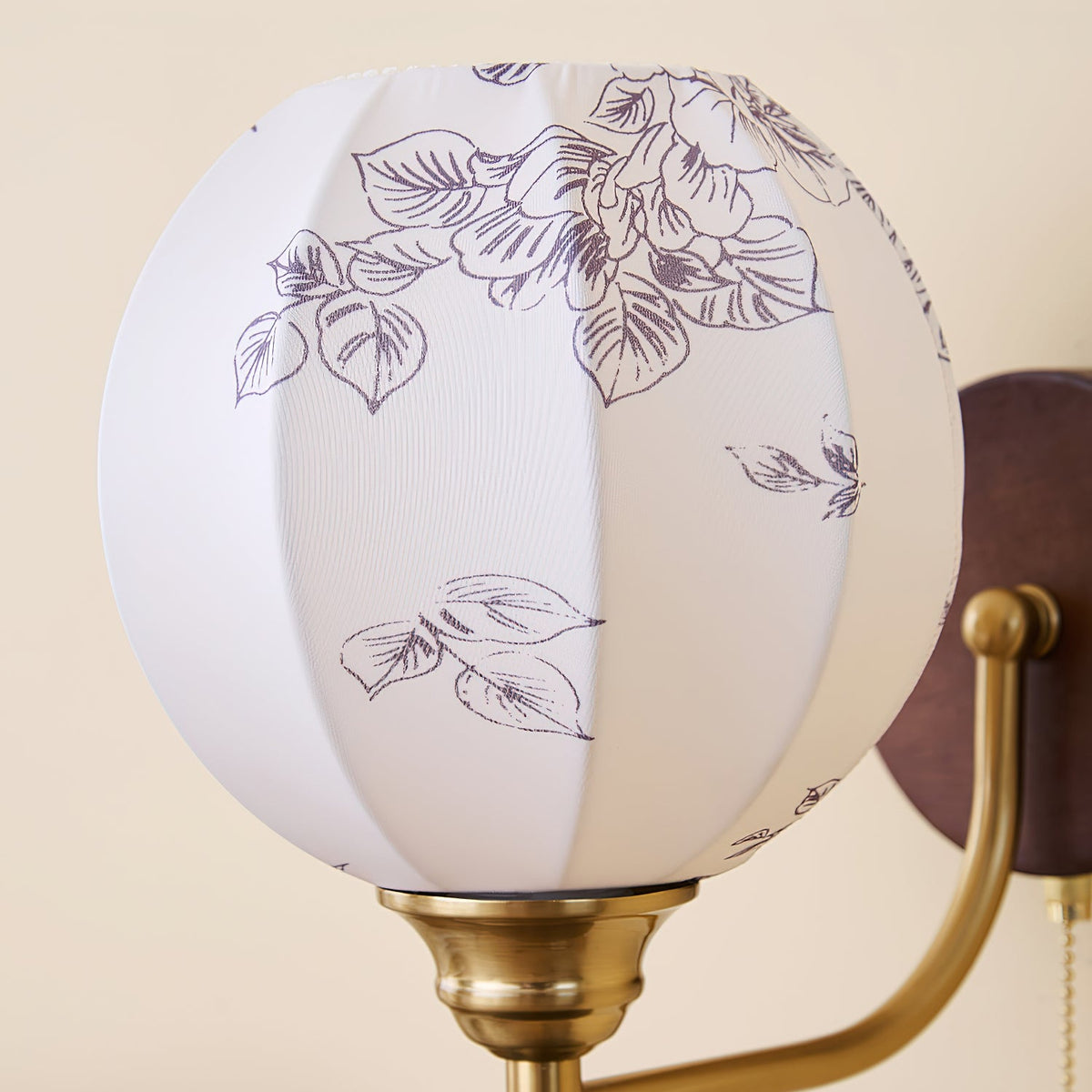 Close view of the globe shade on this Clérachic wall light, showing a purple-grey leaf print on white fabric panels.