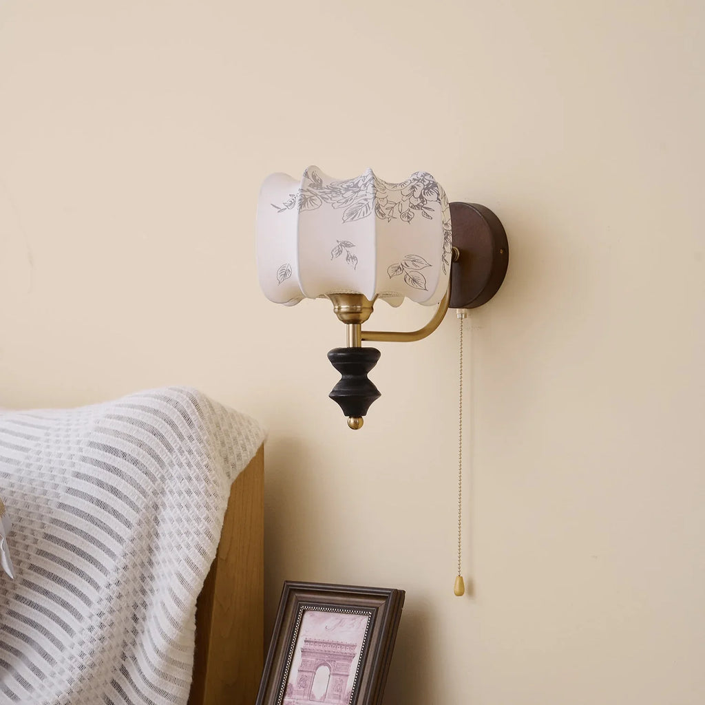 Unlit Clérachic drum-shade wall light with a printed pattern, on a cream wall above a striped throw and a framed print.