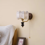 Unlit Clérachic drum-shade wall light with a printed pattern, on a cream wall above a striped throw and a framed print.