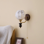 Unlit Clérachic globe wall light with a printed fabric shade on a cream wall, above a striped throw and a framed print.