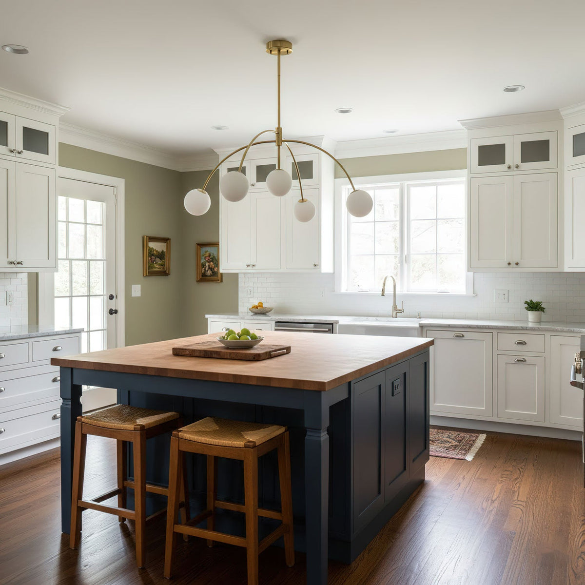 This Clérachic chandelier, in gold, hangs in a kitchen with white cabinets, an island with a wooden top and rattan stools.