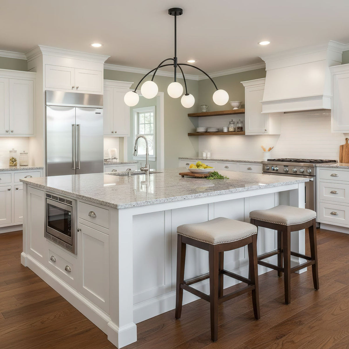Over a white kitchen island with a stone top and cushioned stools, a black Clérachic chandelier carries five lit globes on curved arms.