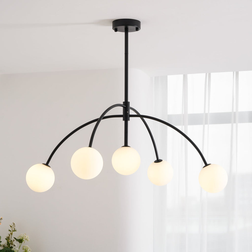 Seen from below, a black Clérachic chandelier with five frosted globes on curved arms, in a bright room with sheer curtains.