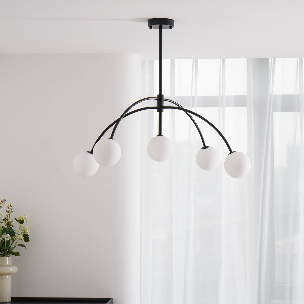 Slightly from below, a black Clérachic chandelier with five milky globes hangs against sheer white curtains, switched off.