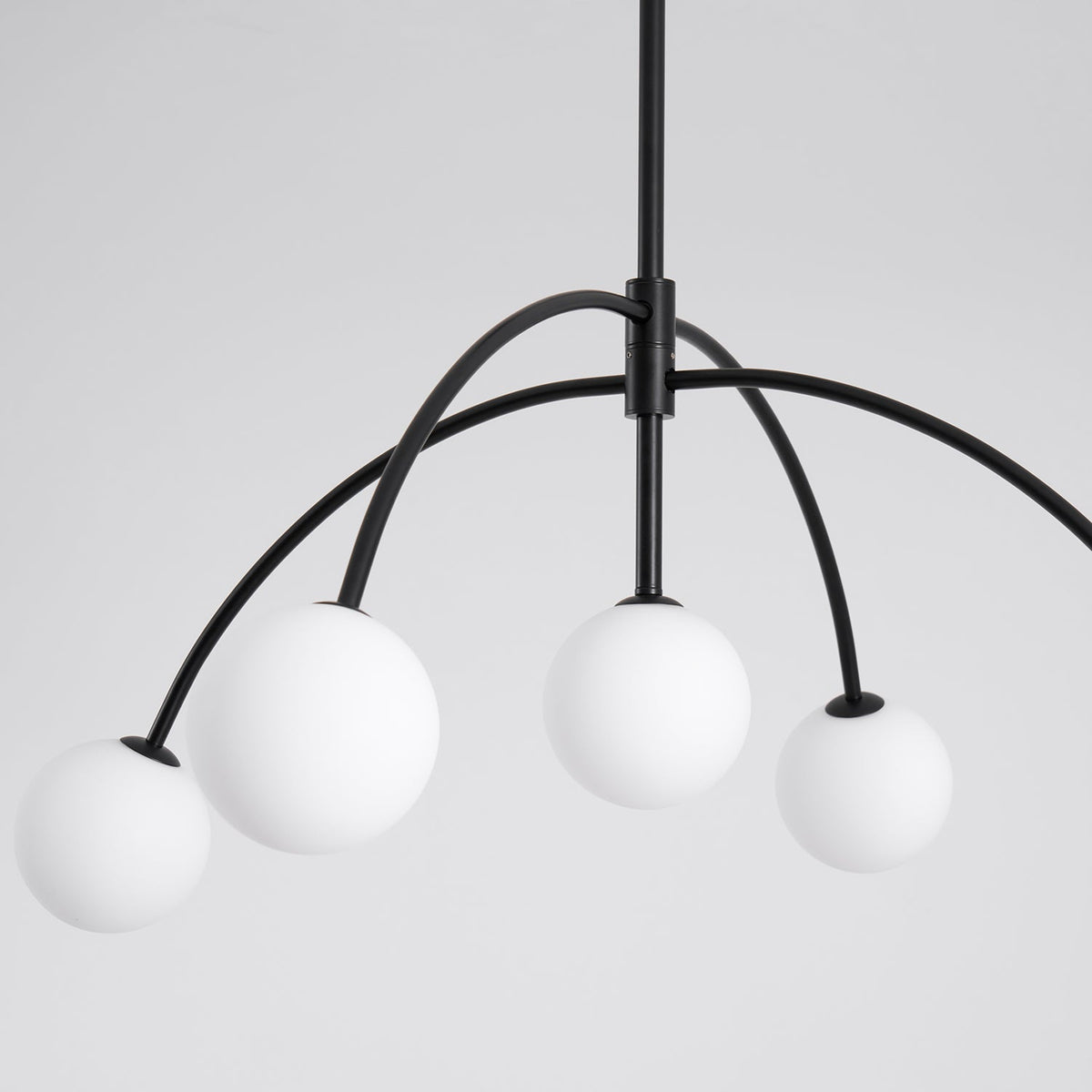 Close view of four frosted globes on curved black arms, joined at a black collar on the central rod of this Clérachic chandelier.