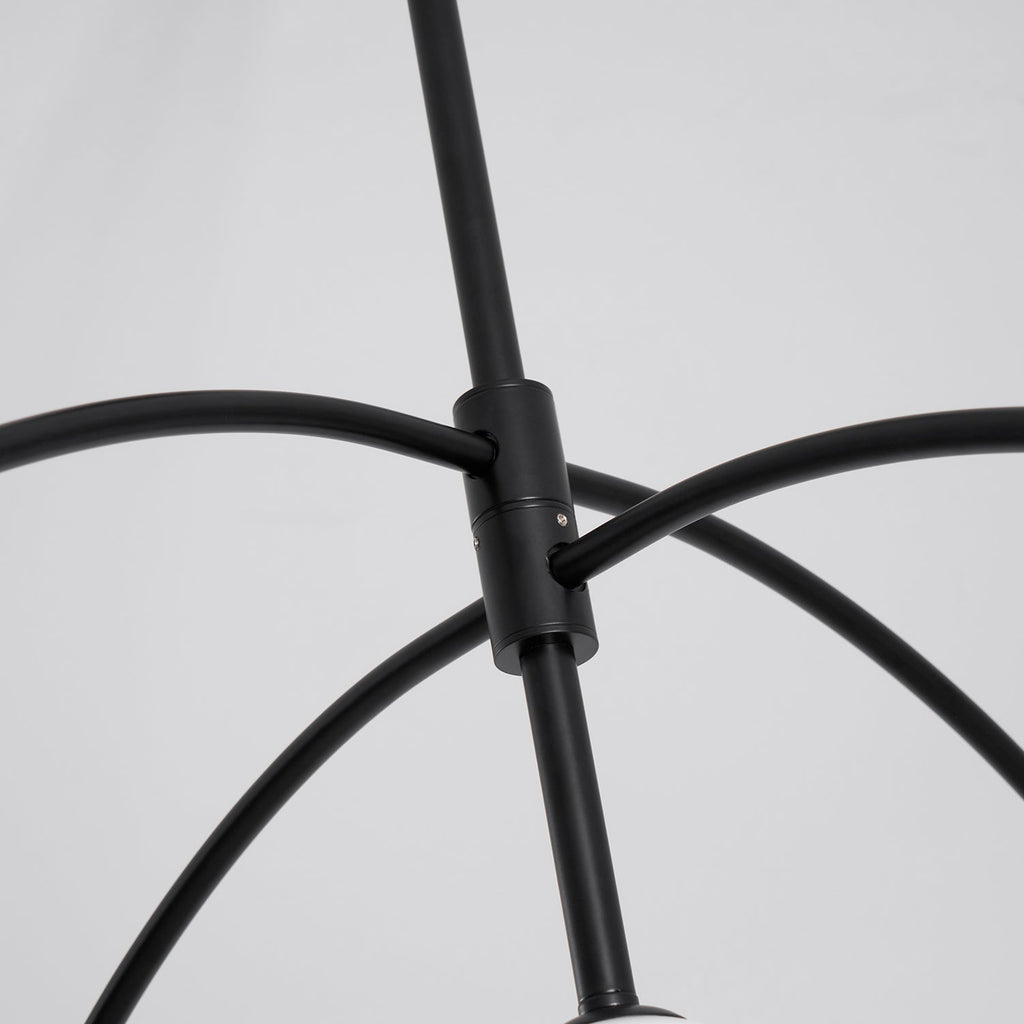 Close view of the black collar where the curved arms meet the central rod of this Clérachic chandelier, on a pale grey backdrop.