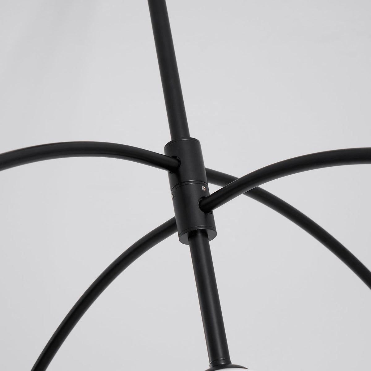 Close view of the black collar where the curved arms meet the central rod of this Clérachic chandelier, on a pale grey backdrop.