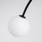 A single frosted white globe with a small black cap, in close view, at the end of a curved arm on this Clérachic chandelier.